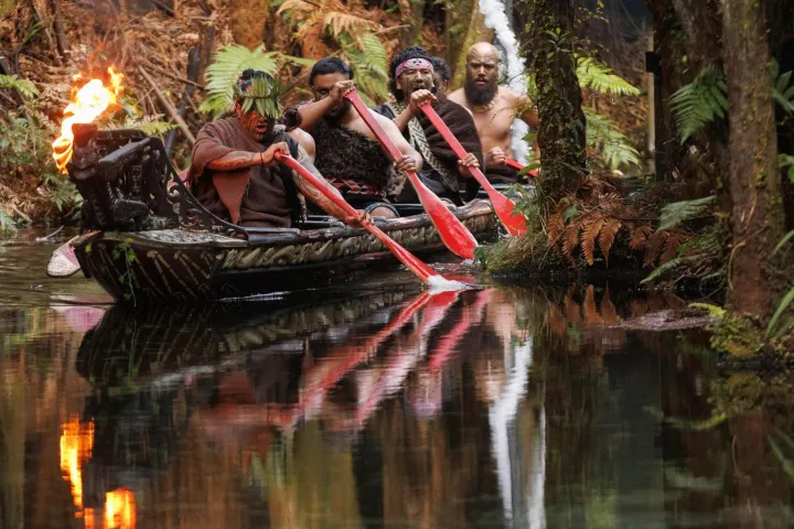 Group paddling a canoe through a lush, forested waterway, one holding a flame.