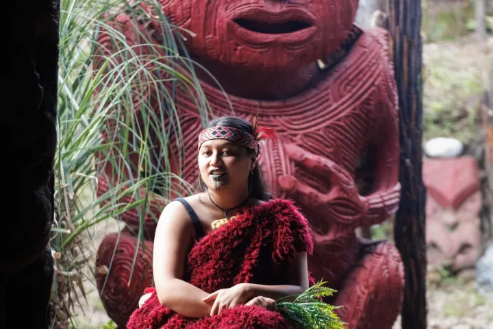 Person in red attire sitting in front of large red carved statue.