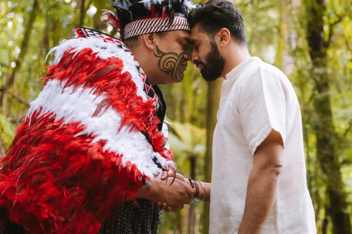 Two men perform a traditional greeting in a forest setting.