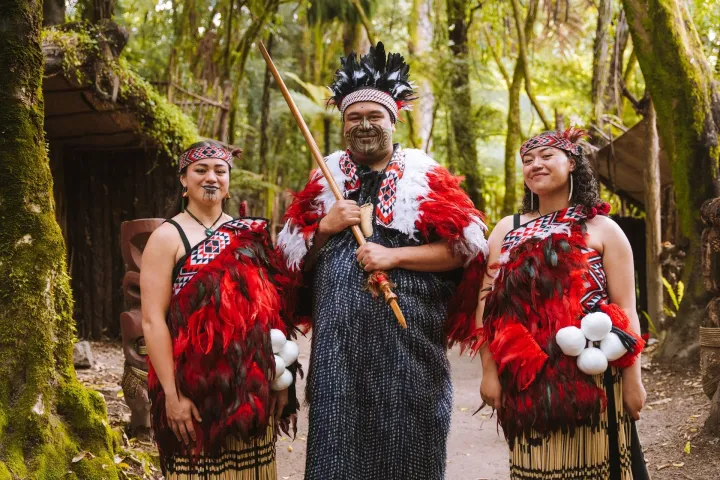 Three people in traditional attire stand in a forest setting.